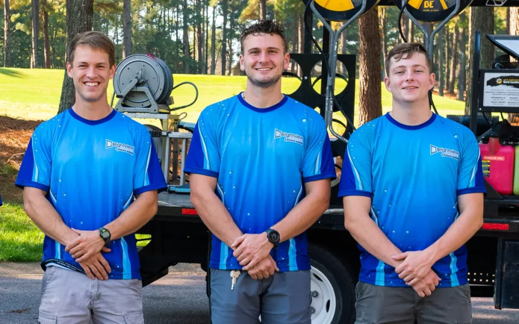 Three smiling Brightview technicians in team shirts in front of the equipment truck