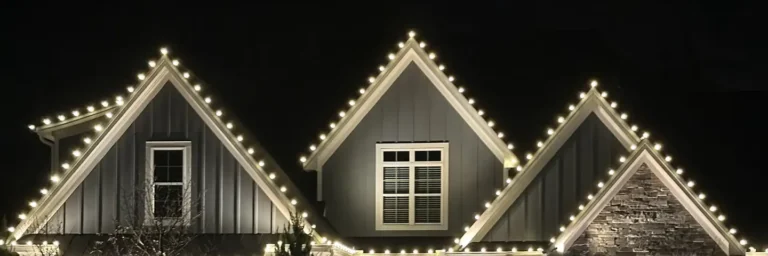 Gabled home outlined in warm white Christmas lights at night