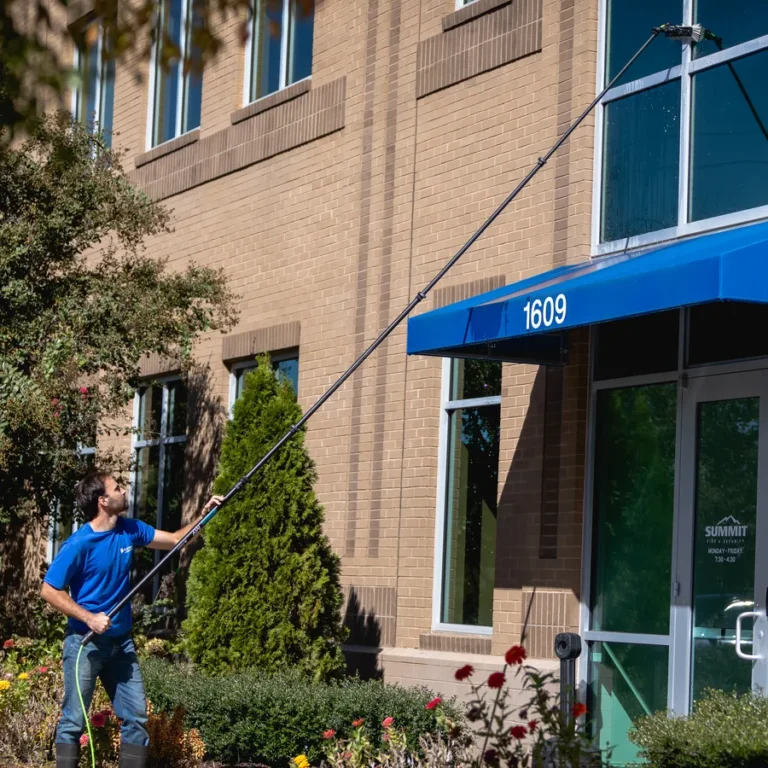 Brightview technician cleaning the upper windows of a brick office building with a water-fed pole