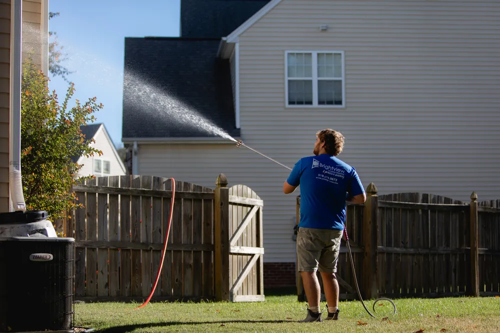 Technician house washing the upper siding of a two-story home from the backyard